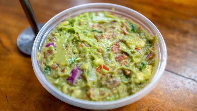 Guacamole in small plastic bowl on wooden table