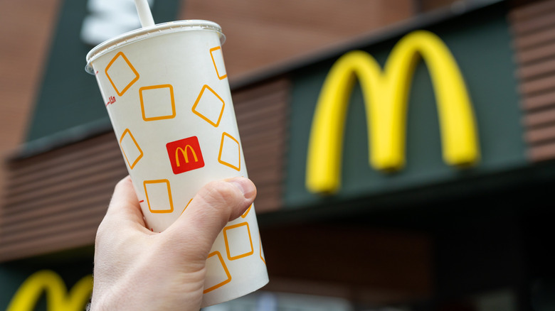 A person holds a McDonald's drink cup in front of a McDonald's sign