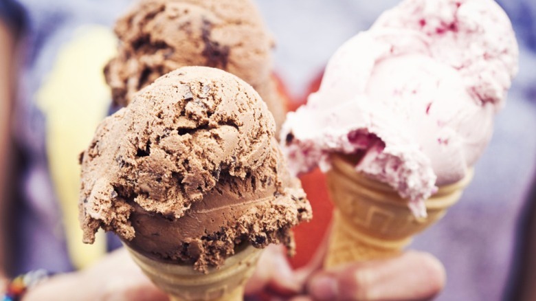 Hand holding chocolate and strawberry ice cream cones.