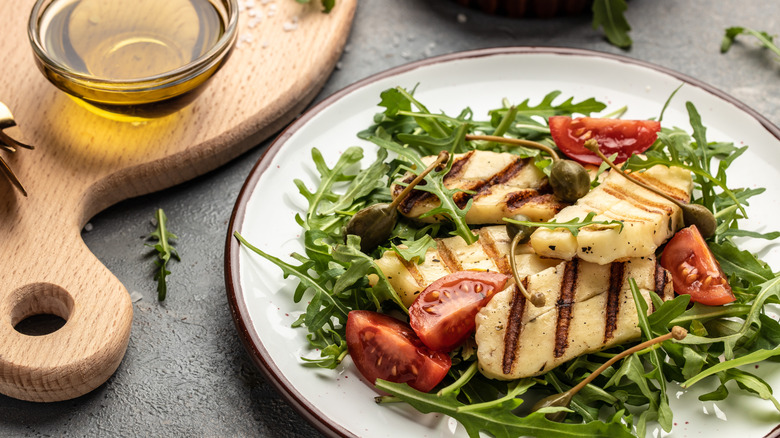 Chicken salad on a white plate with tomatoes, caper berries, and a small bowl of olive oil