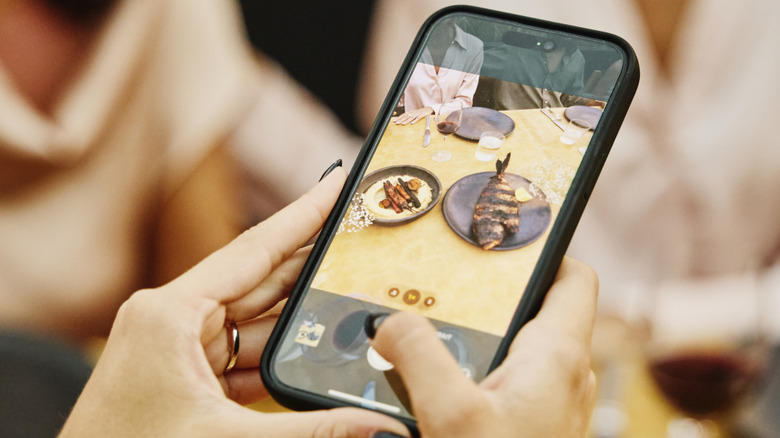 Hands holding a phone photographing grilled fish