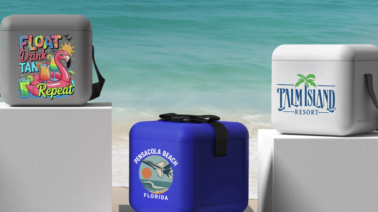 FOAM Coolers with customized designs displayed on top of white boxes placed in front of a shoreline.