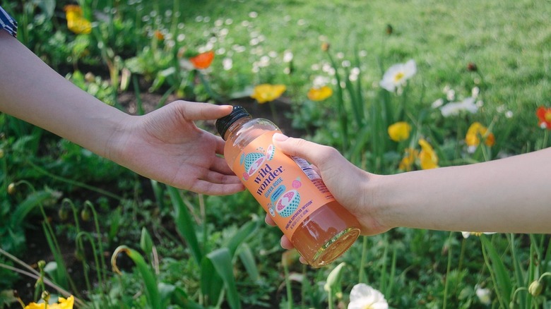 Someone handing another person a bottled-version of the Guava Rose drink