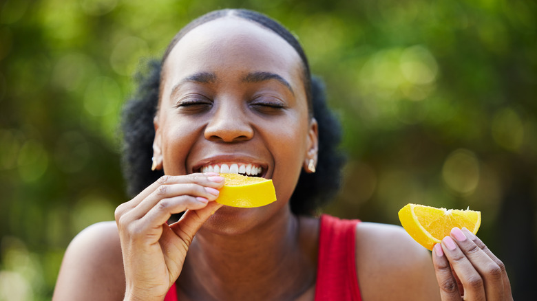 Person's eyes shut biting into an orange slice while holding another slice in other hand