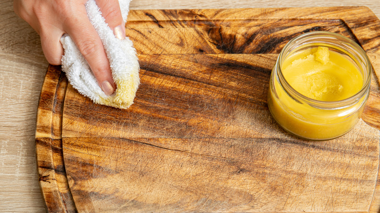 Hands oiling a wooden cutting board with beeswax