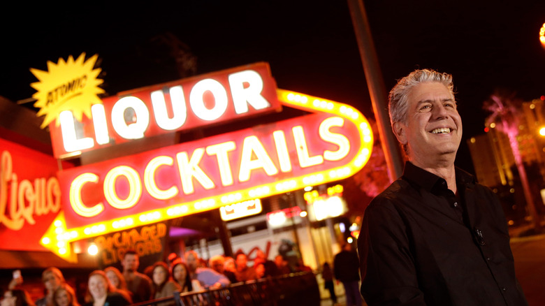Anthony Bourdain standing before a neon sign.