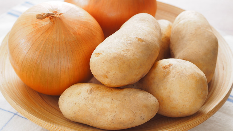 Several potatoes and onions on a wooden plate