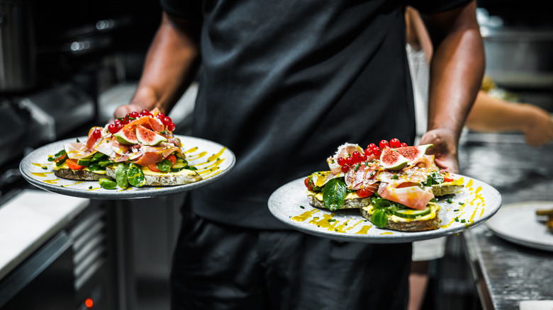 Close up of two plates of food a waiter is carrying out of a restaurant kitchen