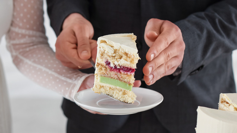 Bride and groom serve a slice of wedding cake on a white plate