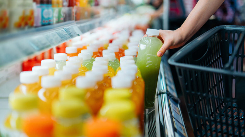 A woman grabs a bottle of juice from a row of beverages