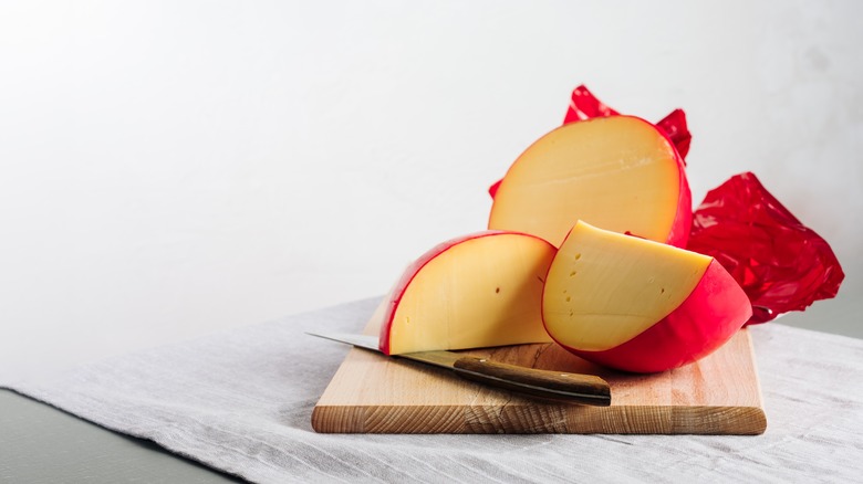 Red wax coated cheese on wooden board with knife
