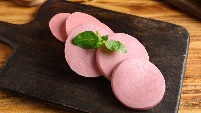 Thick sliced bologna ona  wooden cutting board, topped with a sprig of basil
