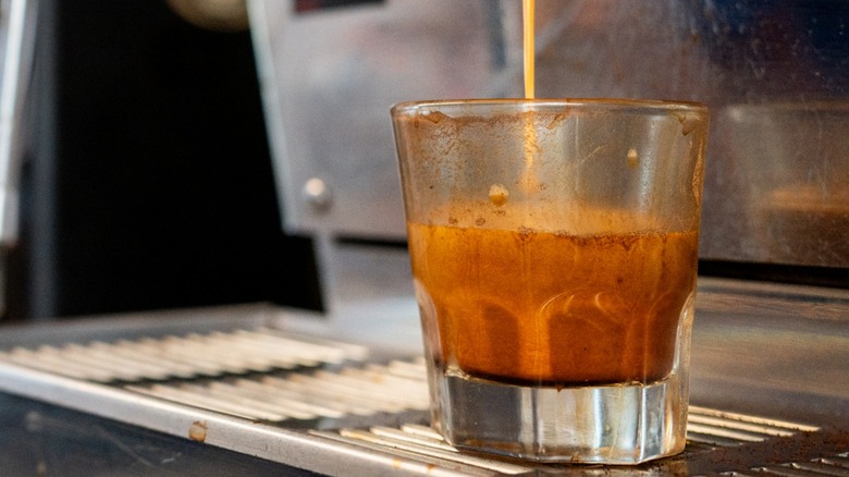 Fresh espresso shot is poured from an espresso machine into a glass