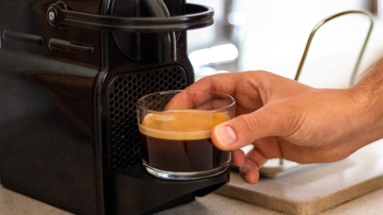 Hand holding freshly brewed espresso from a machine