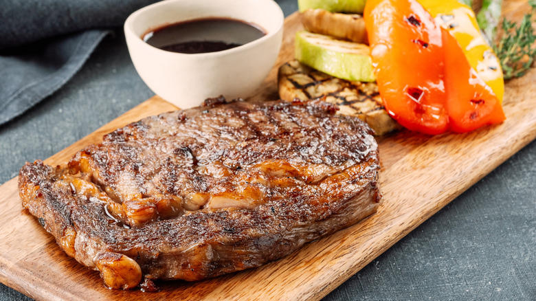 Steak on wooden cutting board with grilled vegetables