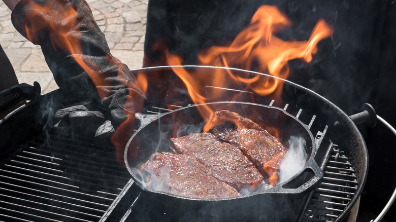 searing three cuts of denver steak in a pan over a flaming grill