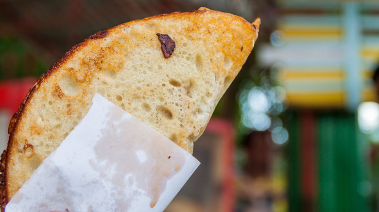 A Cuban personal pizza, folded and held by paper
