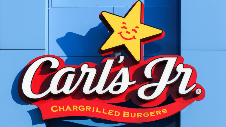 Red and white Carl's Jr. sign with a smiling yellow star on a blue wall