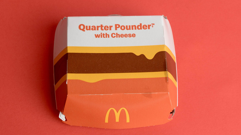 A McDonald's Quarter Pounder with Cheese box on a salmon pink background.