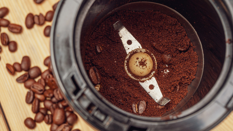 The inside of a coffee grinder containing grinds and whole beans