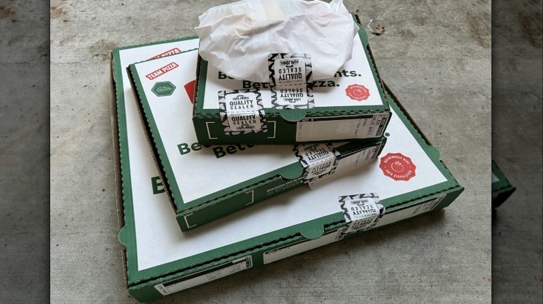 Boxes of Papa John's pizza stacked on a cement floor.