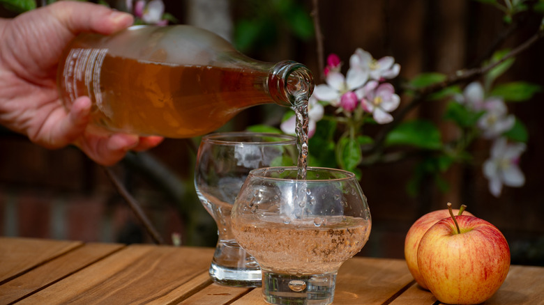 An apple cider being poured from a bottle into a glass on an outdoor table