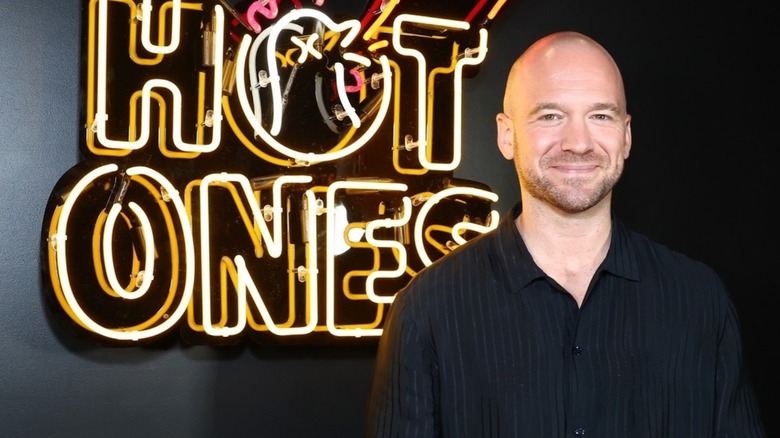 Hot Ones host Sean Evans in front of neon sign