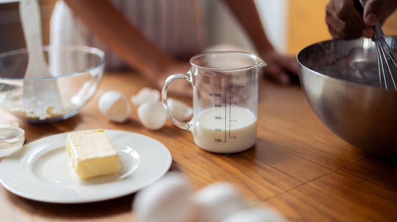Two people stir butter, eggs, and milk in a bowl on a kitchen table