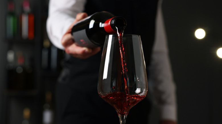 Server pours bottle of red wine into a wine glass