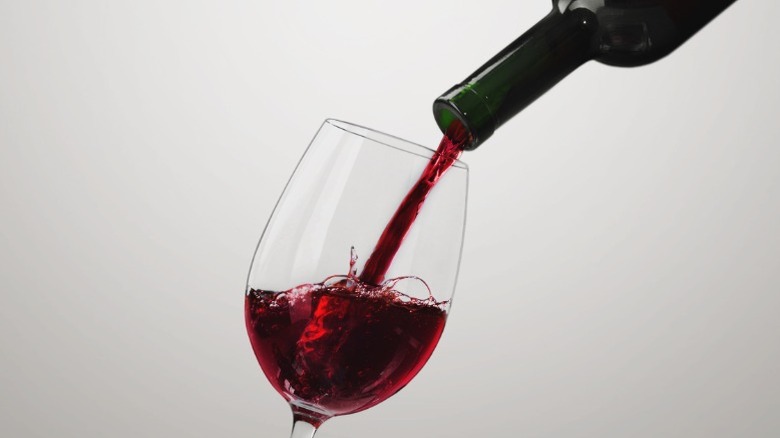 A glass of red wine being poured from a bottle.