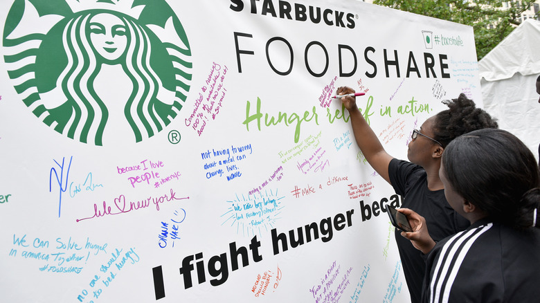 Two people signing board with other signatures advocating for fighting hunger with the Starbucks and FoodShare logo