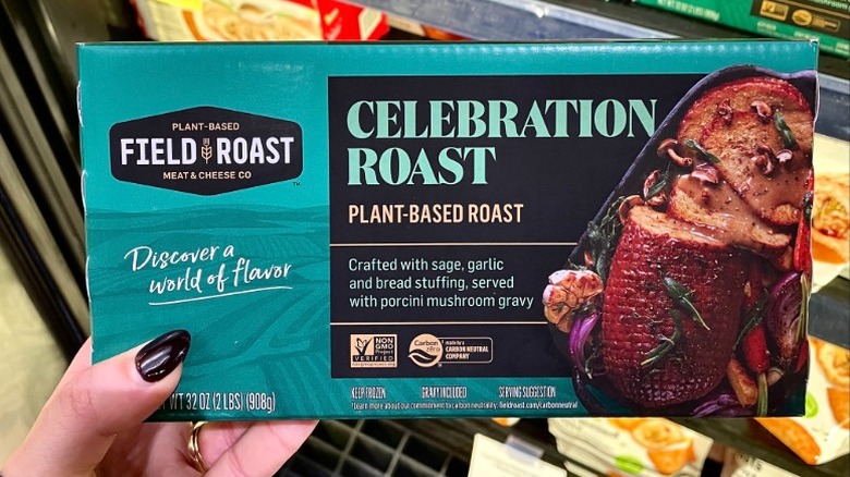a hand holding up a blue package of Field Roast plant-based celebration roast in a grocery store