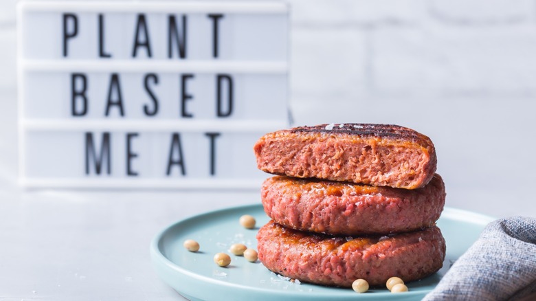a stack of plant-based burger patties on a blue plate in front of a sign that reads 