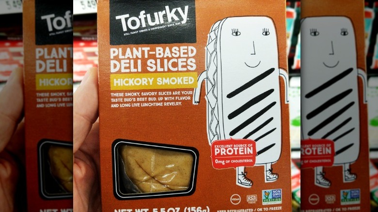 A hand holding up a pack of Tofurky plant-based deli slices in hickory smoked flavor