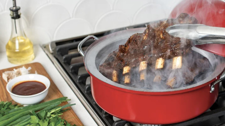 A large cut of bone-in meat being removed from a red smoker with tongs