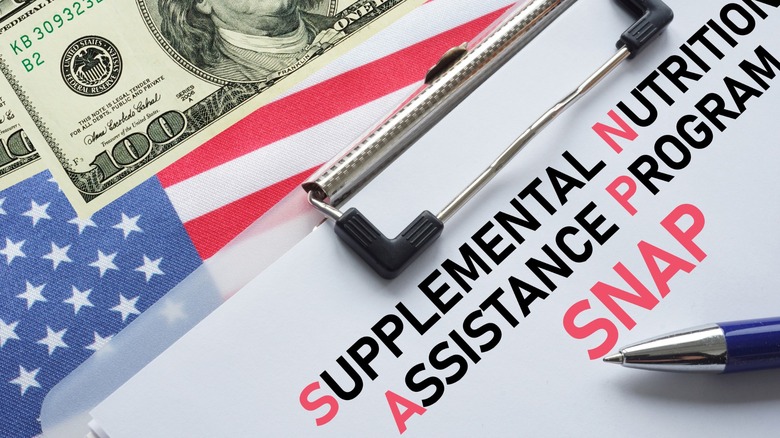 Cash above clipboard holding paper with "Supplemental Nutrition Assistance Program" written on it