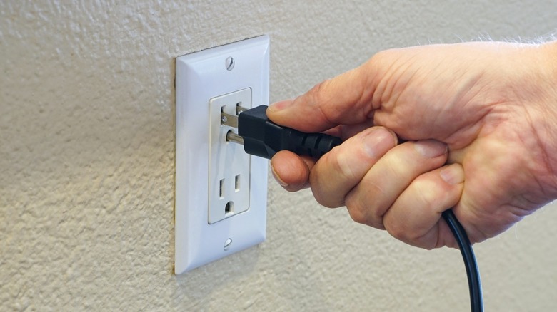 A person removes a plug from an electrical outlet