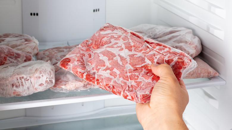 A hand removing a package of ground beef from the freezer.