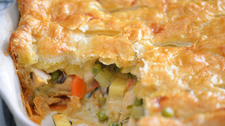 A flaky chicken pot pie cooked in a casserole dish with a scoop taken out.