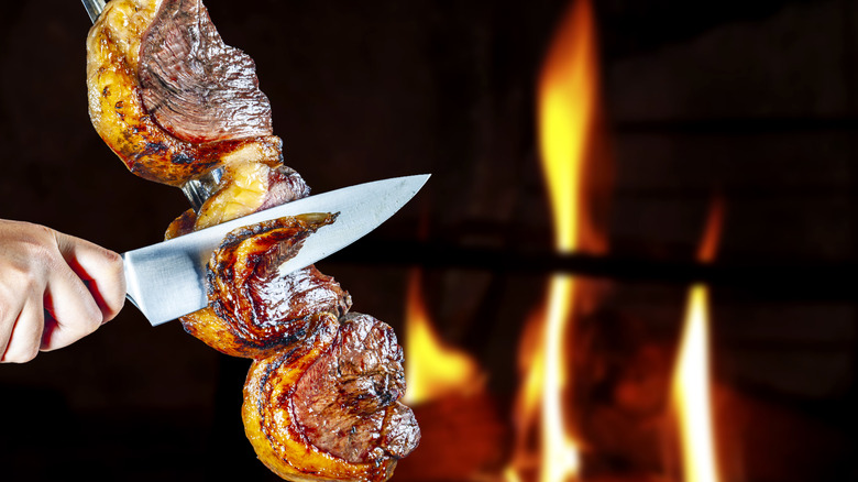 Steak rotisserie at a Brazilian steakhouse with knife slicing picanha off of a skewer