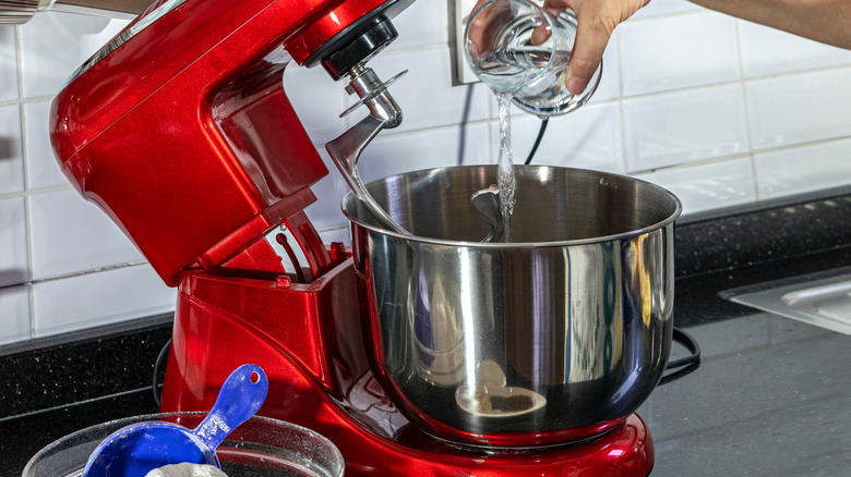 hand pouring water from a glass container into a stand mixer bowl
