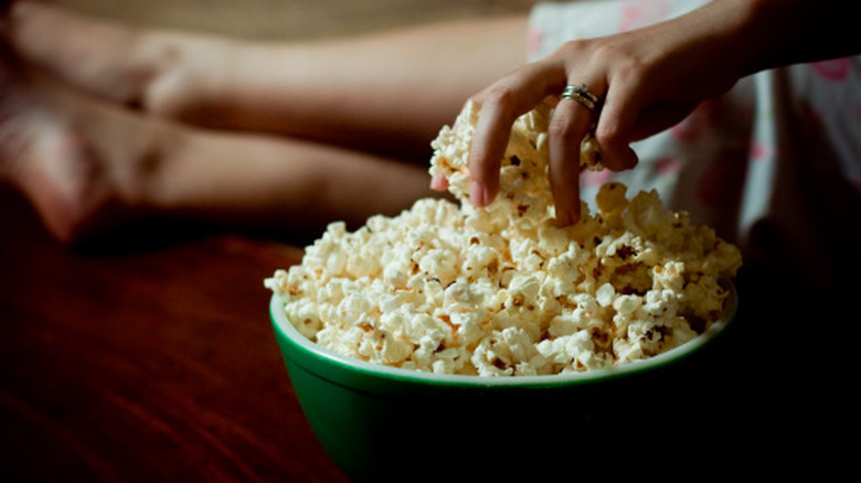 A person reaching into a green bowl full of popcorn