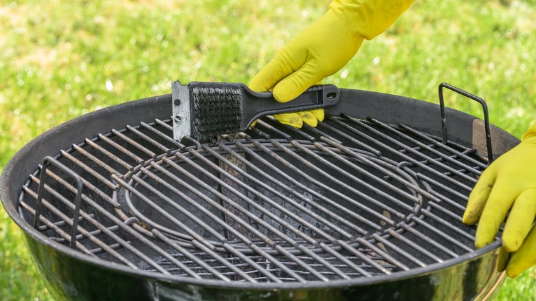 Person wearing gloves holding a grill scraper over a charcoal grill