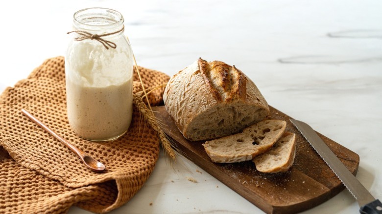 A sourdough starter next to a loaf of sourdough bread