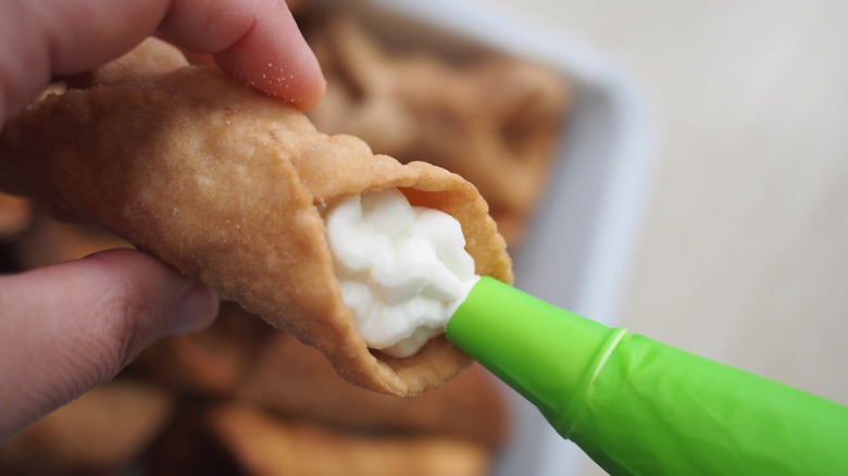 A person pipes filling into a cannoli pastry shell