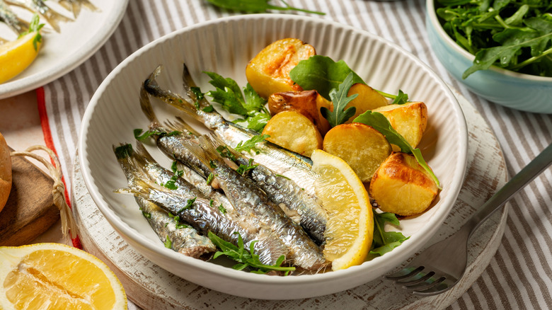 Sardines in a bowl with lemon, potatoes, and arugula