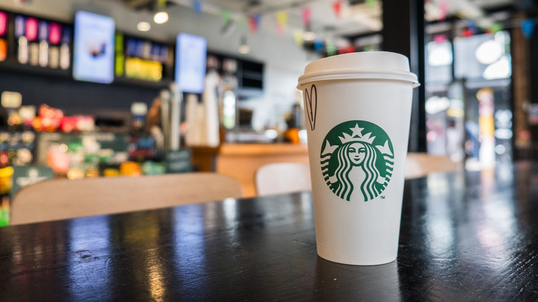 A Starbucks drink in a white paper cup on a table inside the restaurant