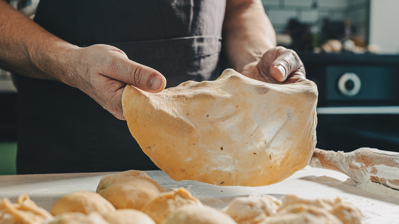 Hands shaping dough over a floured surface with more dough