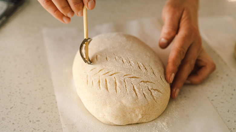 A baker scoring bread dough on a floured parchment paper