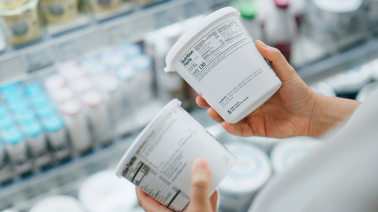Person comparing two containers of yogurt in each hand